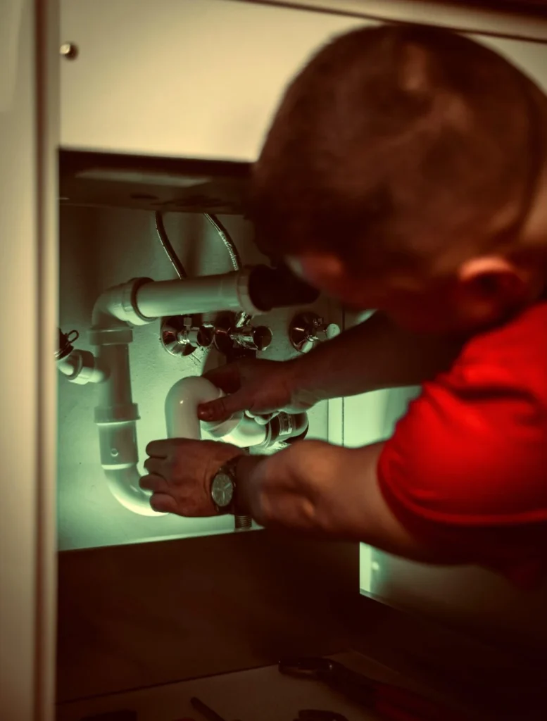 A plumber reaching under a sink to fix the pipes, standing in for the systems work Kingster Local's process automation handles.