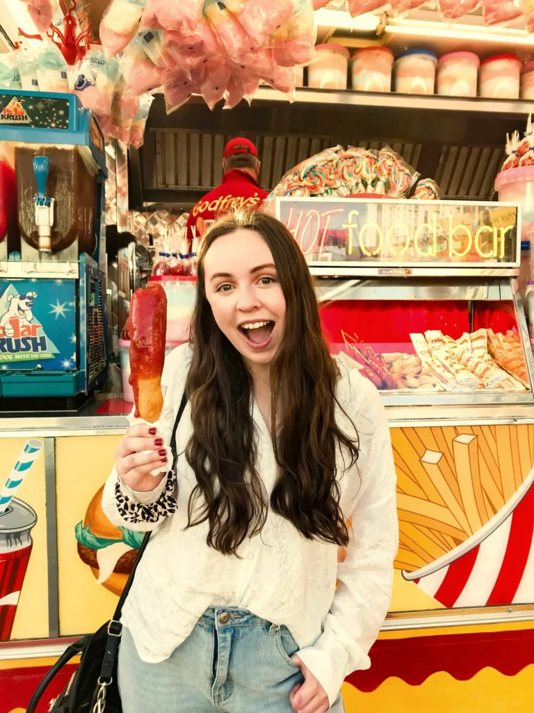 A woman grinning and holding up a corn dog at a fair, the kind of customer delight Kingster Local's review automation captures.