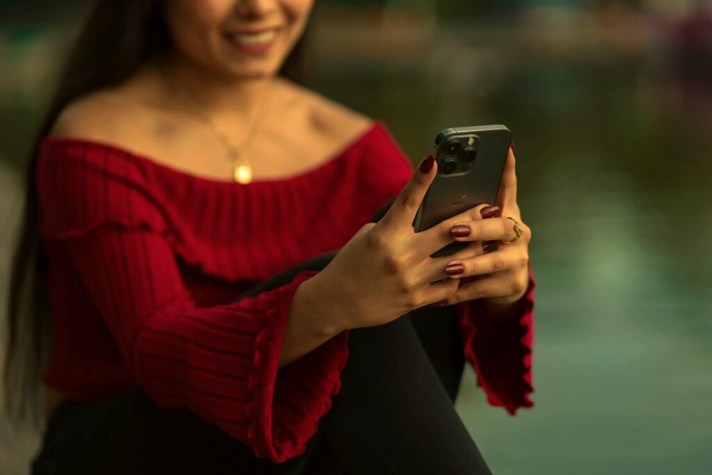 Woman happily looking at her phone, off-shoulder red top, warm bronze grade
