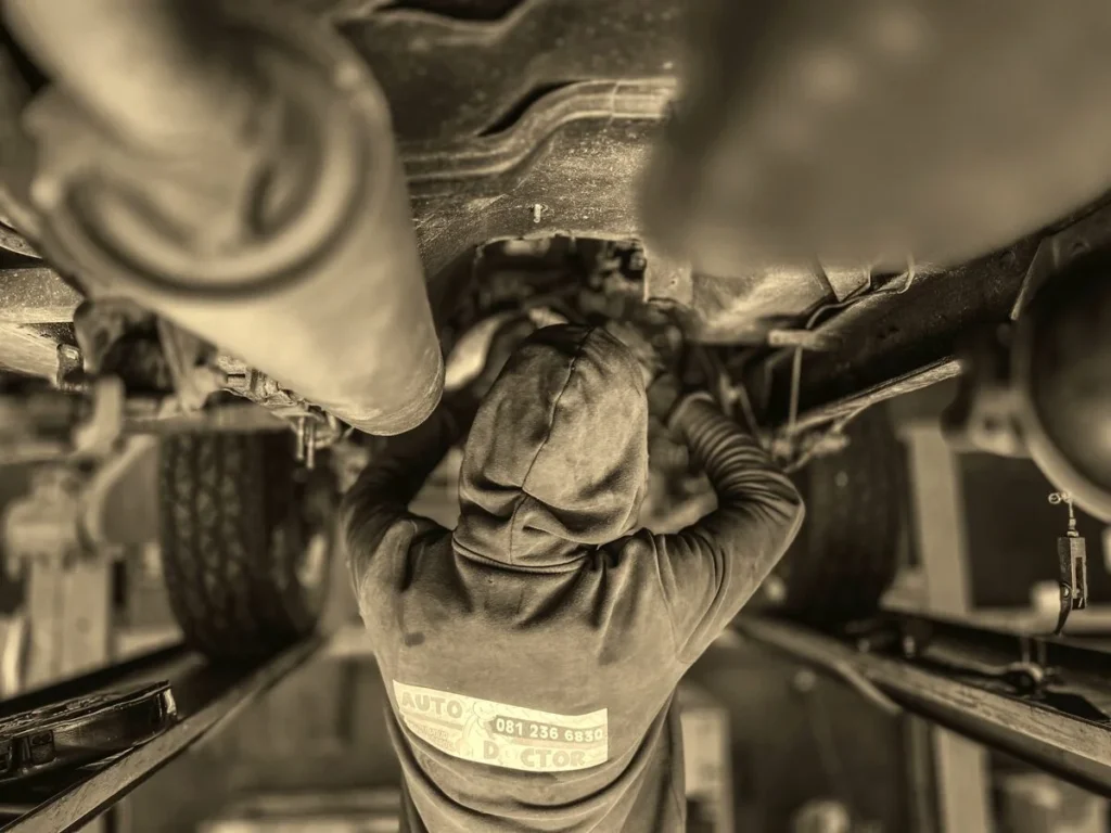A mechanic working underneath a car at an 'Auto Doctor' shop, standing in for the under-the-hood app work Kingster Local handles.