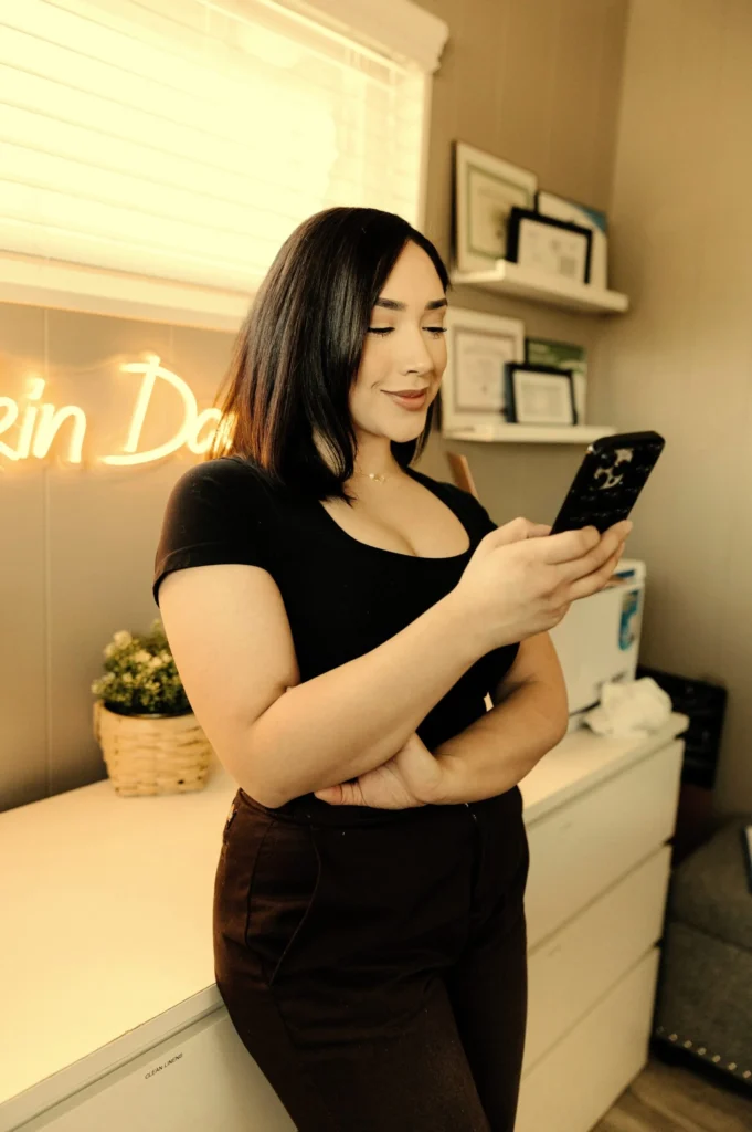 A woman checking her phone in a softly lit studio, capturing the on-the-go feel of Kingster Local's social media management.